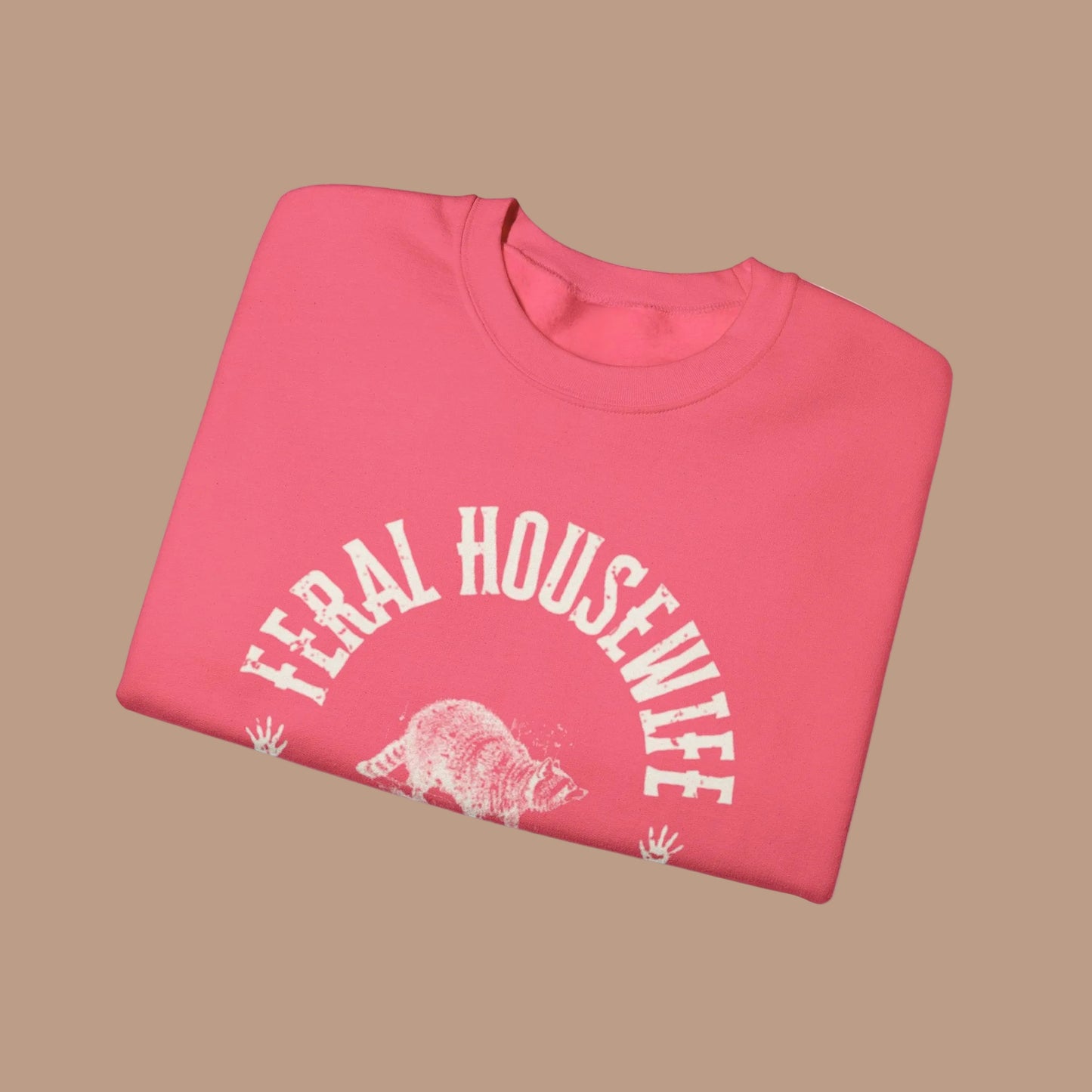 Folded pink sweatshirt with 'Feral Housewife' text and graphic on a white background