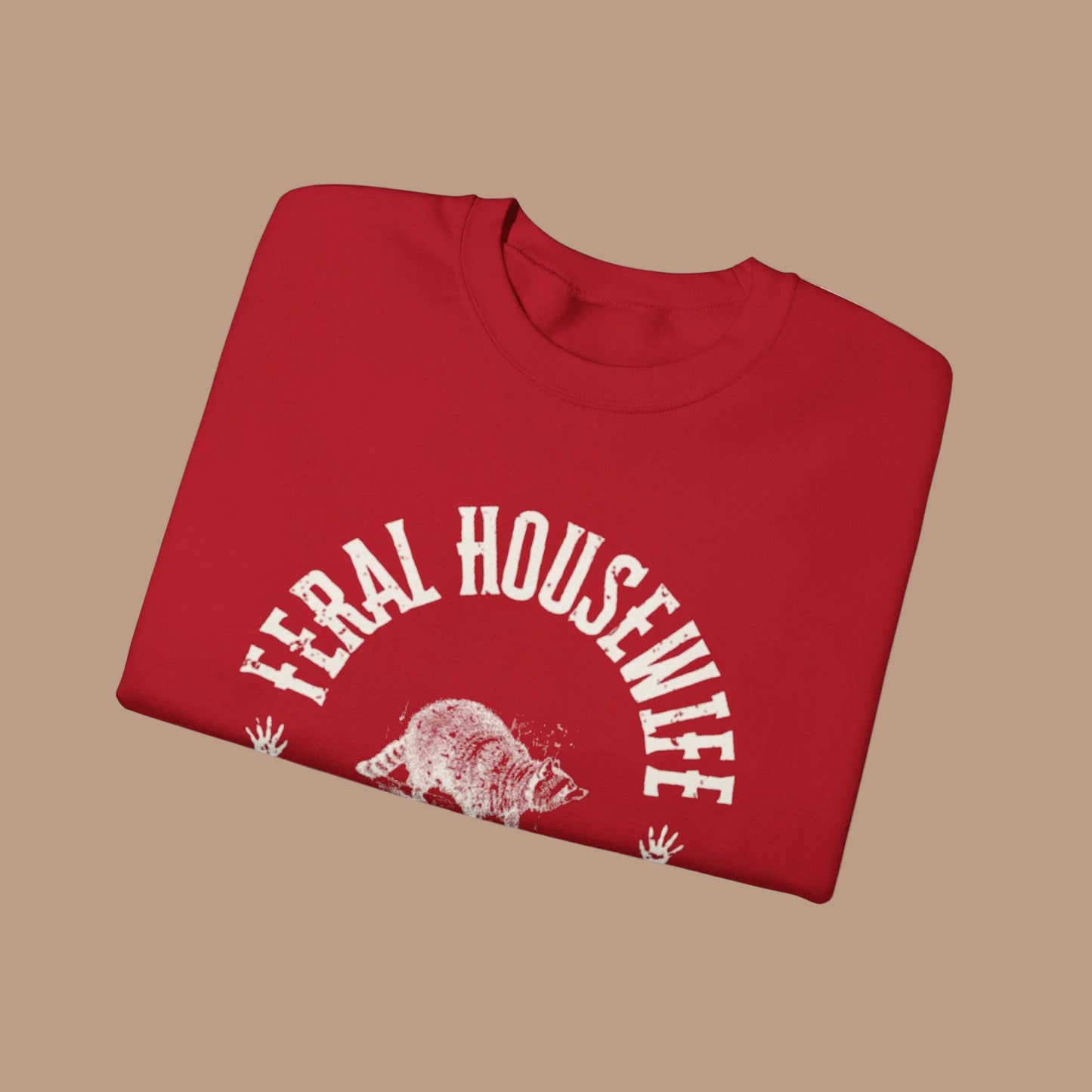 Folded red sweatshirt with 'Feral Housewife' text and graphic on a white background