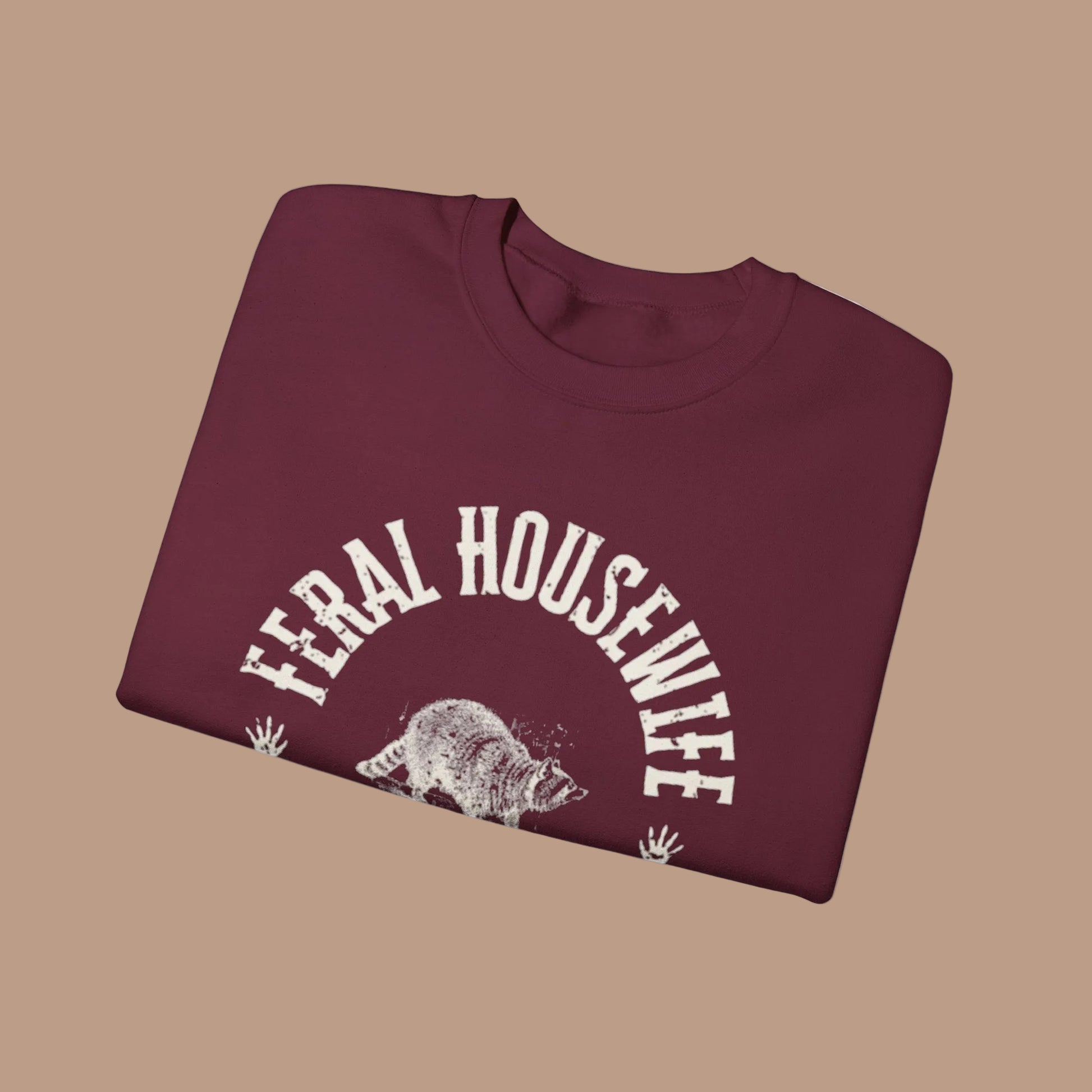Folded maroon sweatshirt with 'Feral Housewife' text and graphic on a white background
